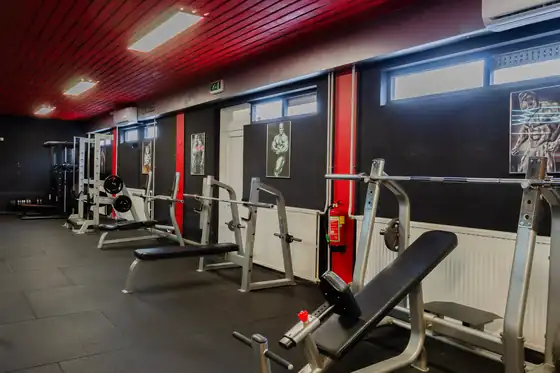 Bankjes en racks onder het rode plafond bij Xplosive Gym Helmond